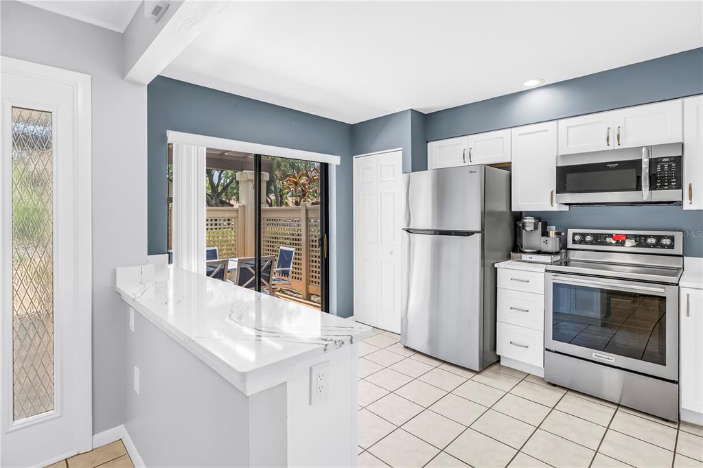 A kitchen with white cabinets, stainless steel appliances, a marble-look countertop, and a sliding door — 3174 WINDRUSH UNIT 25, SARASOTA, FL
