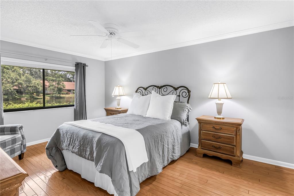 A bedroom features a bed with gray bedding, two wooden nightstands, and a window view — 3174 WINDRUSH UNIT 25, SARASOTA, FL