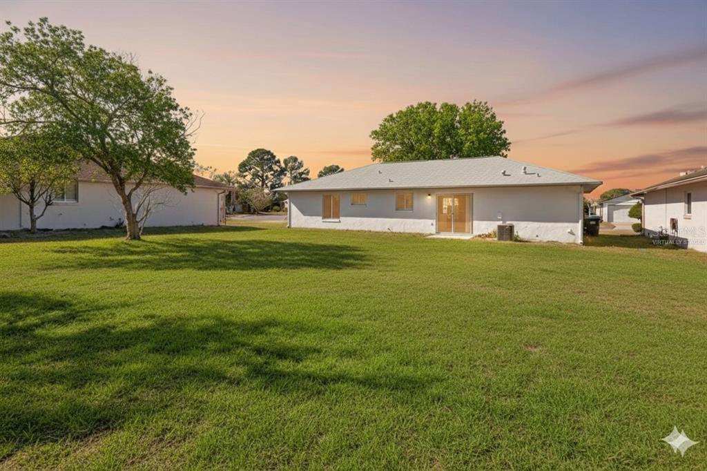 The exterior of a white single-story house with a large grassy backyard and trees — 11407 SPLITWOOD LANE, ORLANDO, FL