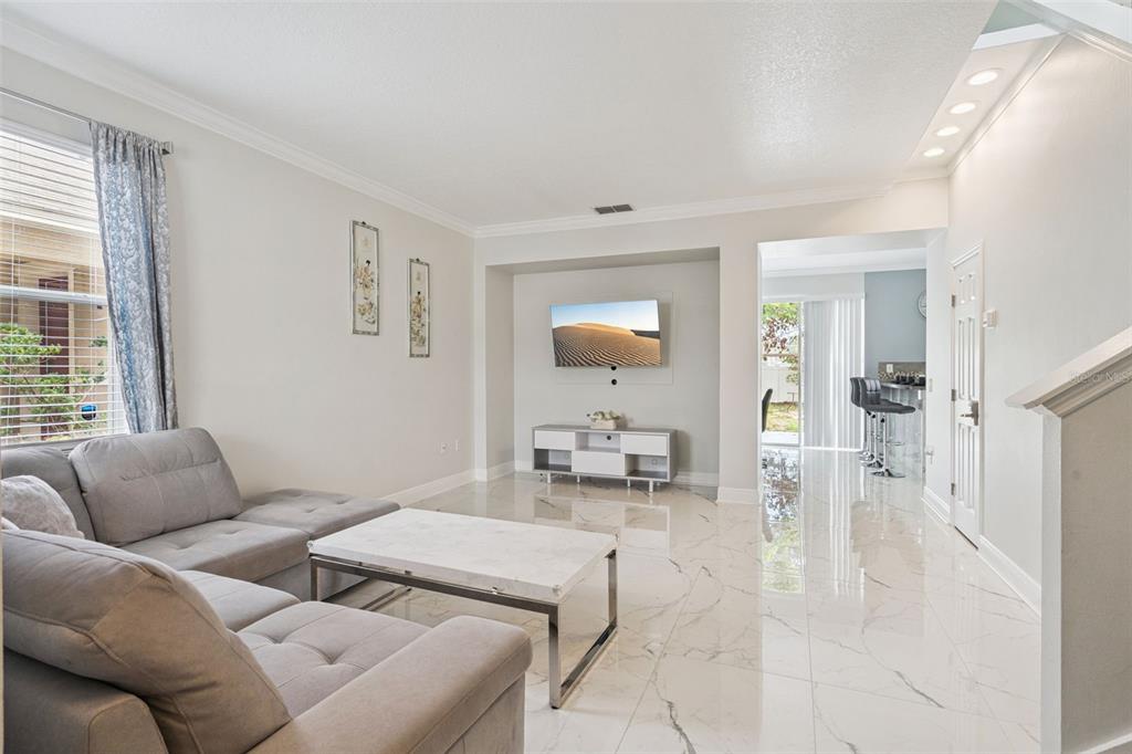 A living room features light gray walls, white marble-look tile flooring, and a wall-mounted television — 233 ROSSELLI BOULEVARD, DAVENPORT, FL