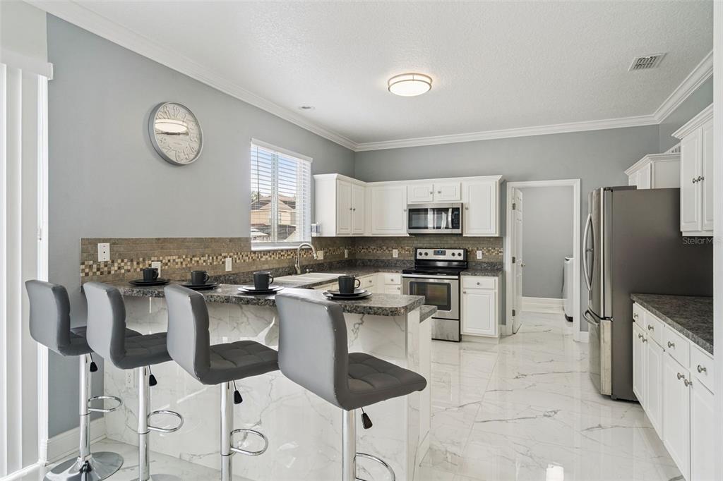 A kitchen features white cabinets, granite countertops, a marble-patterned island with bar stools, and tile flooring — 233 ROSSELLI BOULEVARD, DAVENPORT, FL