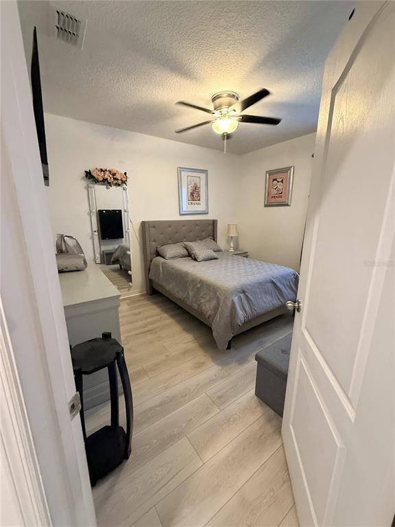 A bedroom features a tufted headboard, light wood-look flooring, and a ceiling fan — 329 WINGED ELM DRIVE, DEBARY, FL