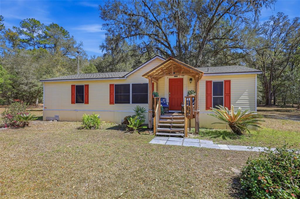 A yellow manufactured home with red shutters and a wooden front porch sits outdoors — 1131 SW 166TH STREET, NEWBERRY, FL