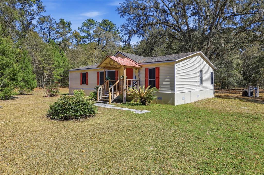 A single-story manufactured home with light siding, red shutters, and a small wooden front porch — 1131 SW 166TH STREET, NEWBERRY, FL
