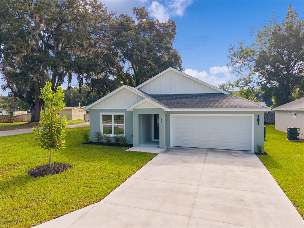 A single-story house with light green siding, a white garage door, and a concrete driveway — 768 POWELL STREET, WILDWOOD, FL