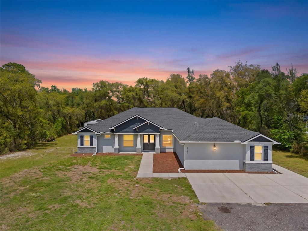 A single-story house with a gray exterior, dark roof, and a concrete driveway at sunset — 11099 YELLOW HAMMER ROAD, WEEKI WACHEE, FL