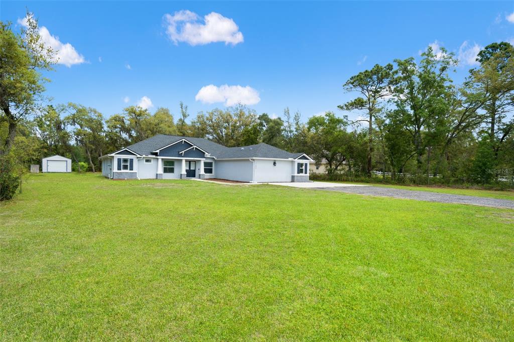 A single-story house with a gray exterior and a gravel driveway sits on a lawn — 11099 YELLOW HAMMER ROAD, WEEKI WACHEE, FL