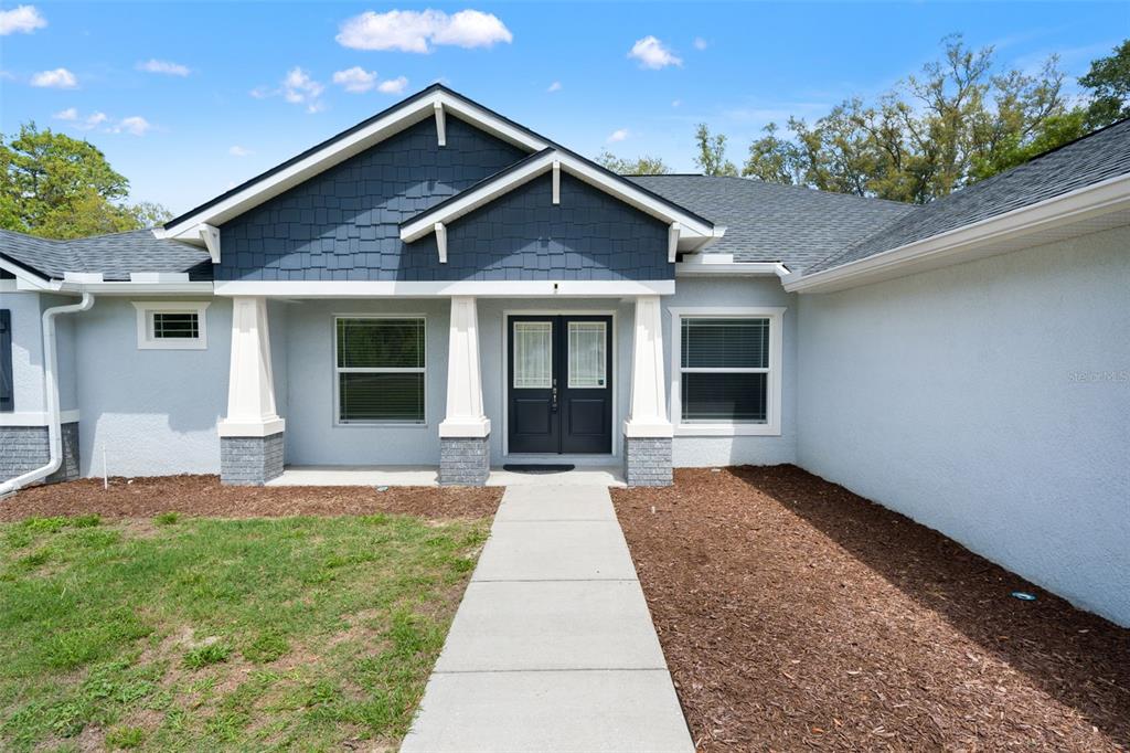 The exterior of a house features a blue shingled gable, white columns, and a walkway — 11099 YELLOW HAMMER ROAD, WEEKI WACHEE, FL