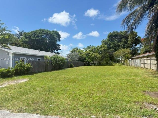 A vacant grassy lot sits between two houses with wooden fences under a blue sky — 213 NW 12th St, Pompano Beach FL 33060, POMPANO BEACH, FL