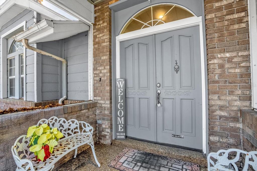 A gray double front door with a transom window sits between brick walls and siding — 3500 SAIL FISH AVENUE, FRUITLAND PARK, FL