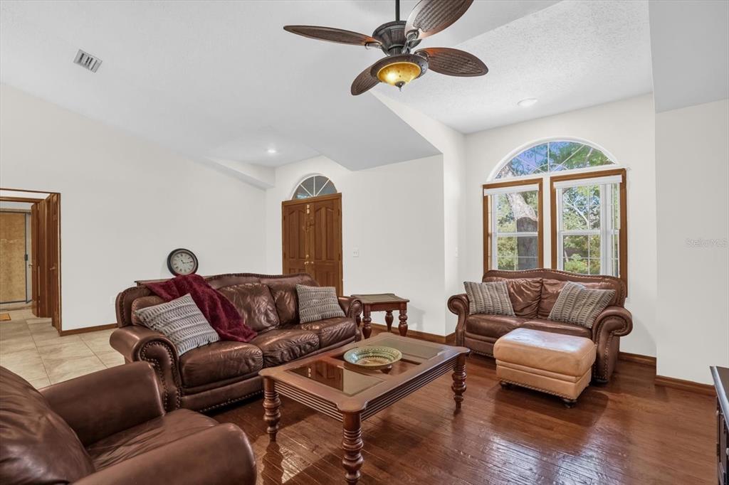 A living room features dark leather furniture, hardwood floors, a ceiling fan, and arched windows — 3500 SAIL FISH AVENUE, FRUITLAND PARK, FL