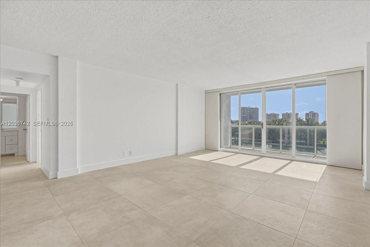 An empty room features large light-colored floor tiles, white walls, and a sliding glass door — 9381 E Bay Harbor Dr # 404S, Bay Harbor Islands FL 33154, BAY HARBOR ISLANDS, FL