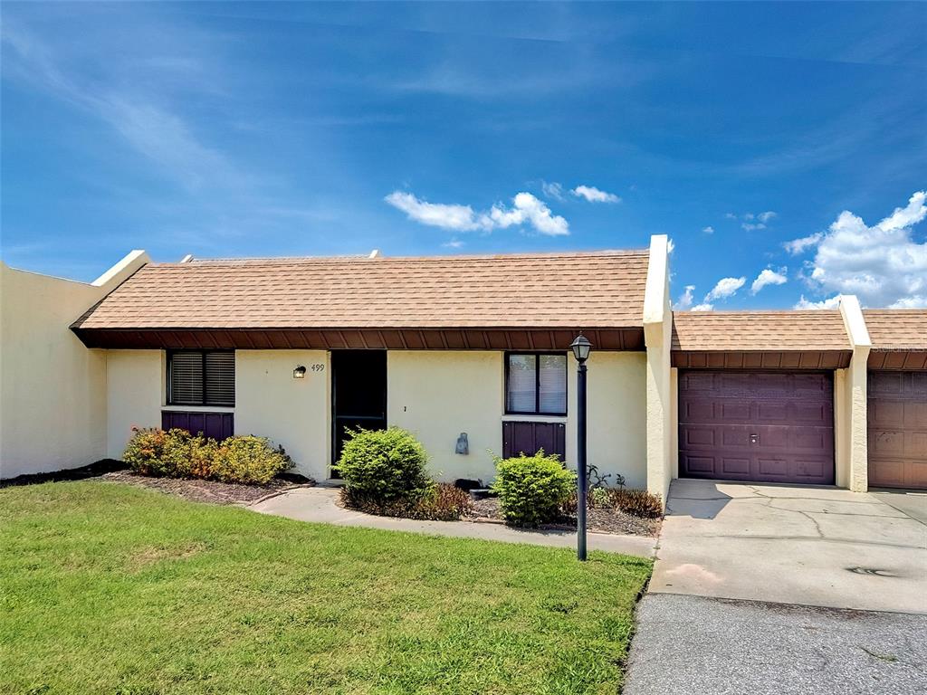 A single-story townhouse with a tan stucco exterior, brown shingle roof, and attached garage — 499 ALBEE FARM ROAD UNIT V11, VENICE, FL