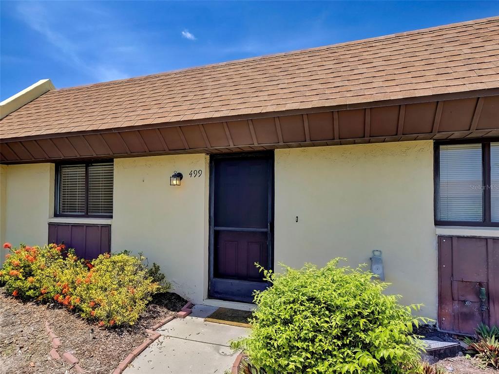 A single-story building exterior features a brown shingled roof, beige walls, and a front door — 499 ALBEE FARM ROAD UNIT V11, VENICE, FL