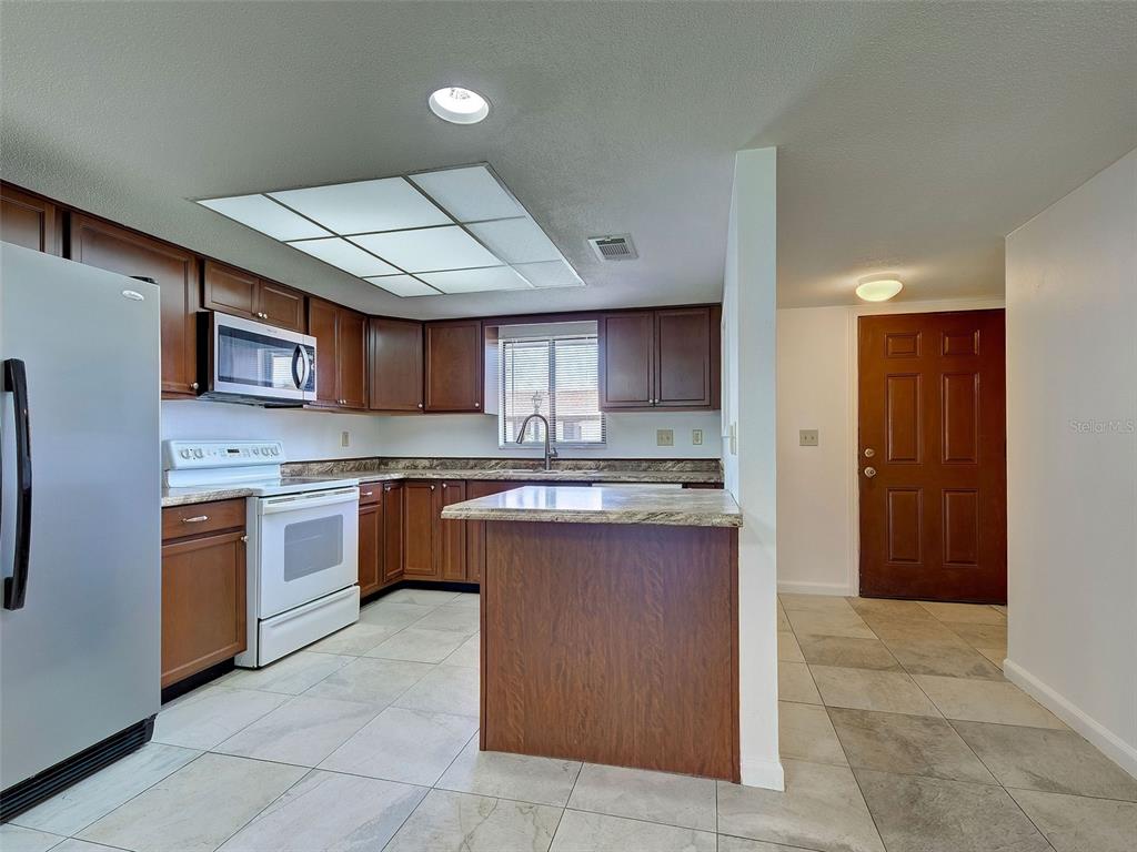 A kitchen features wood cabinets, granite countertops, a kitchen island, and tile flooring — 499 ALBEE FARM ROAD UNIT V11, VENICE, FL
