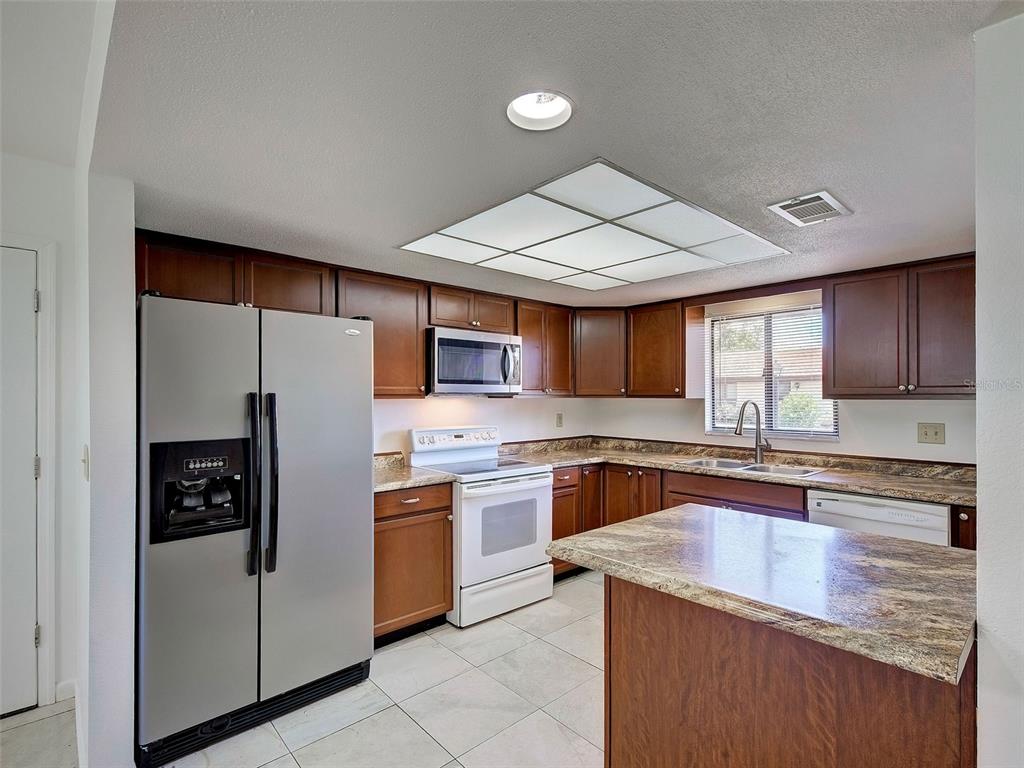 A kitchen features wood cabinets, stainless steel appliances, granite countertops, and a tile floor — 499 ALBEE FARM ROAD UNIT V11, VENICE, FL