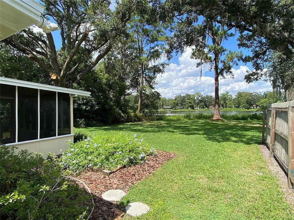 A grassy backyard features a screened porch, a flower bed, and a view of water — 1025 LAKE JESSAMINE DRIVE, ORLANDO, FL