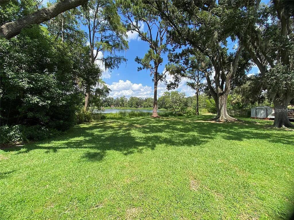 A grassy backyard features mature trees and a view of a lake in the distance — 1025 LAKE JESSAMINE DRIVE, ORLANDO, FL