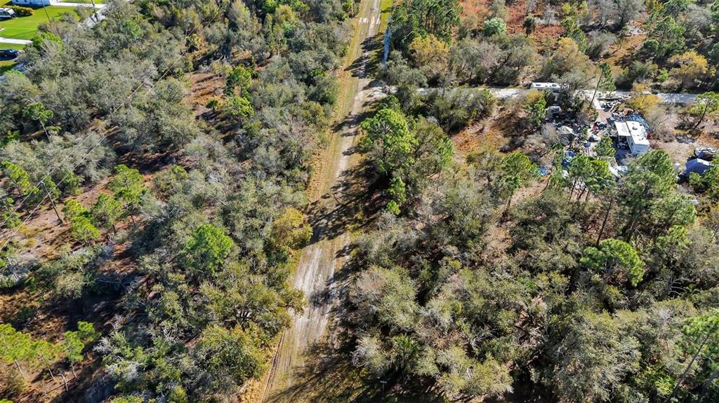 An aerial view shows a dirt path running through a wooded area with nearby residential structures — 13142 BANYAN DRIVE, PUNTA GORDA, FL