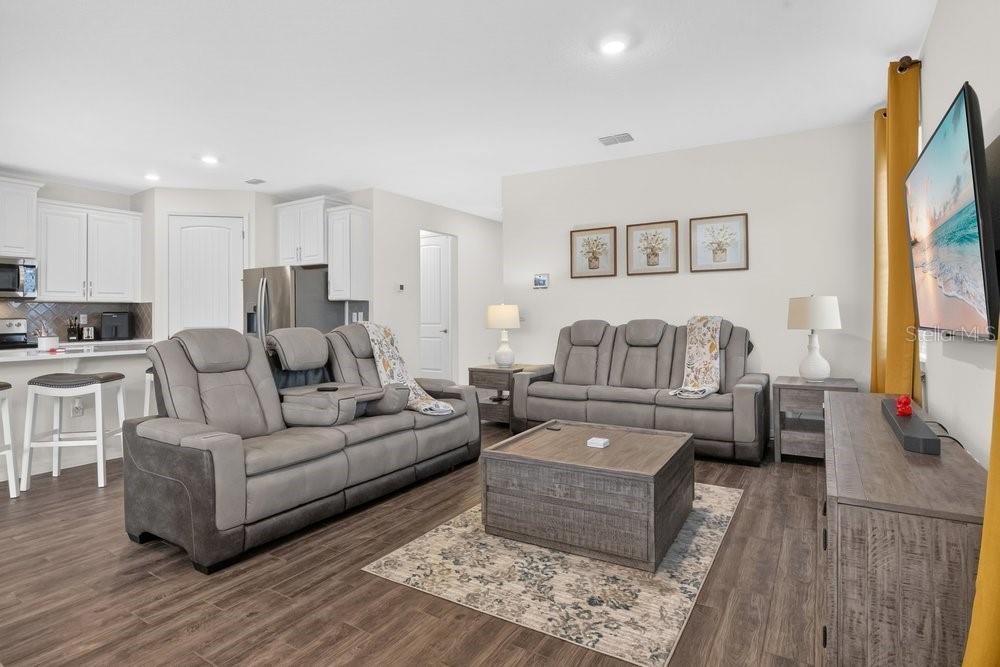 A living room features gray sofas, a wooden coffee table, and an open-concept kitchen — 17718 BLAZING STAR CIRCLE, CLERMONT, FL