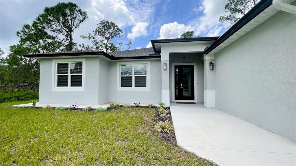 The exterior of a light-colored house features a covered entryway and two windows — 3399 LA GOY STREET, NORTH PORT, FL