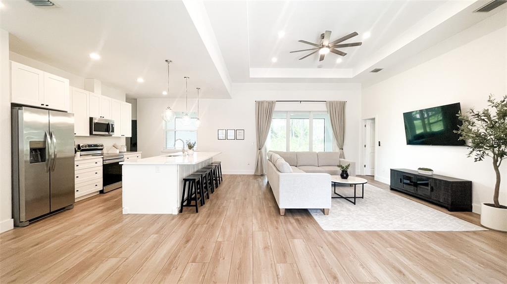 An open-concept kitchen and living area features white cabinetry, a kitchen island, and wood-look flooring — 3399 LA GOY STREET, NORTH PORT, FL