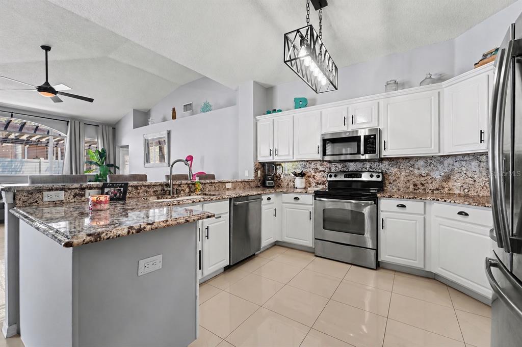 A kitchen features white cabinets, granite countertops, stainless steel appliances, and a large island — 19717 WYNDHAM LAKES DRIVE, ODESSA, FL