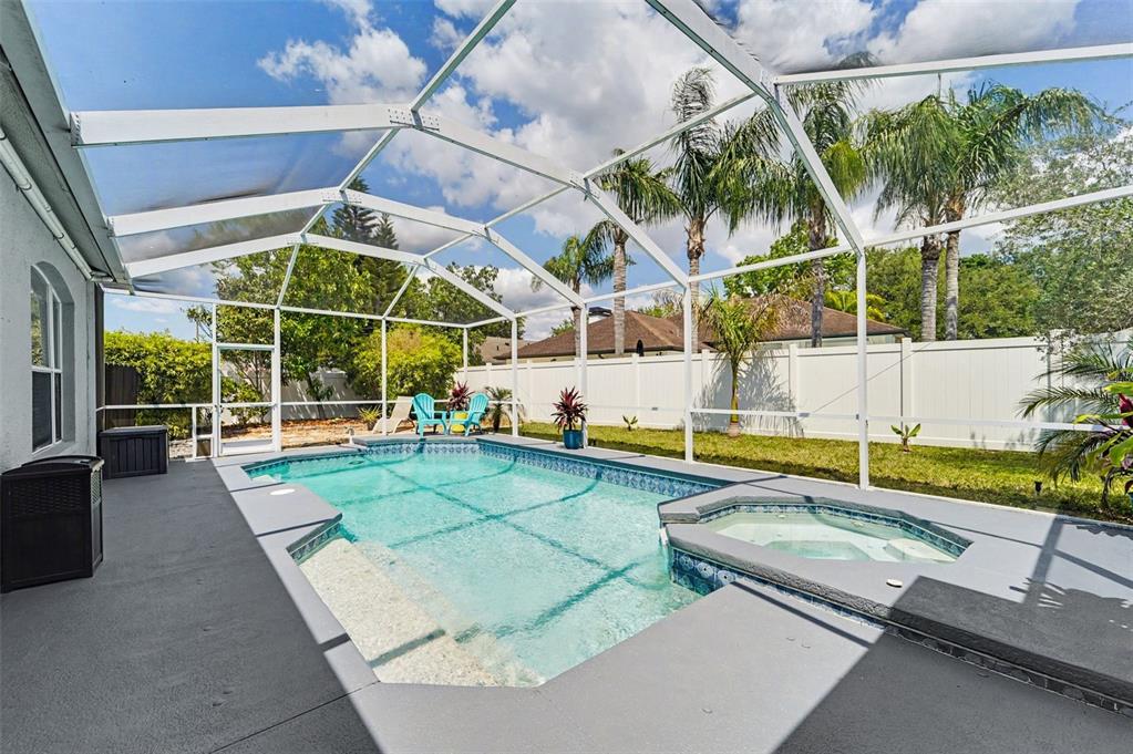 A screened-in swimming pool and hot tub sit on a gray patio in a backyard — 19717 WYNDHAM LAKES DRIVE, ODESSA, FL
