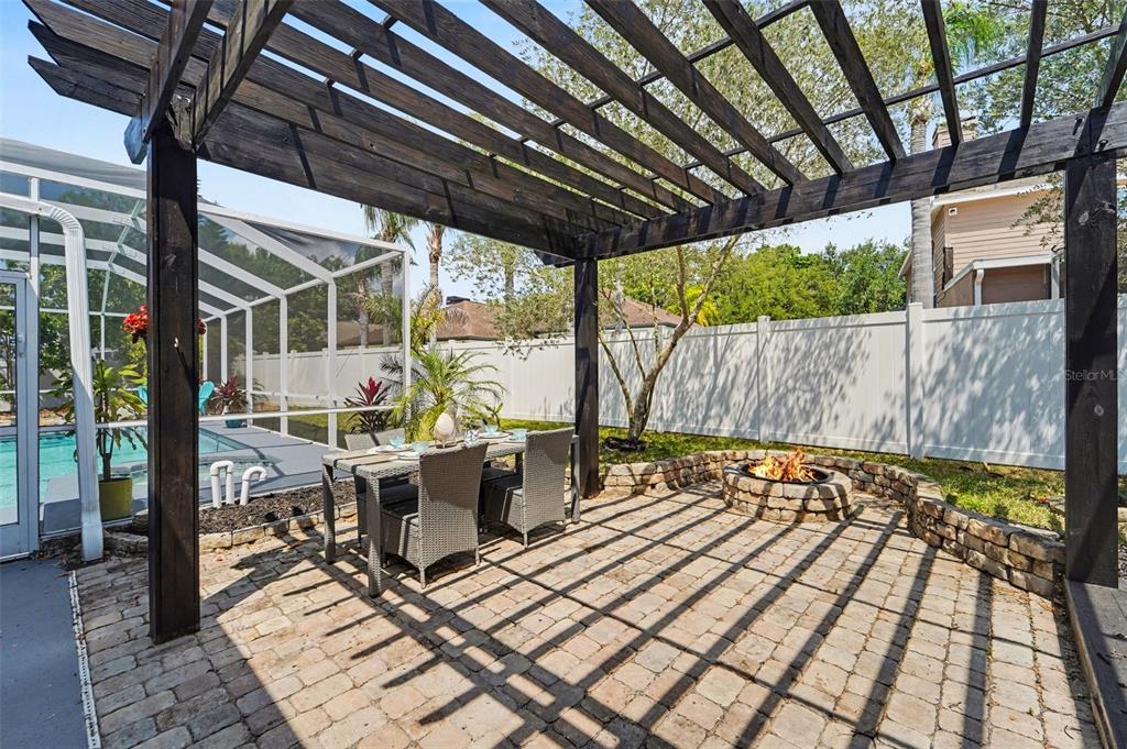 A backyard patio features a wooden pergola, a dining set, and a stone fire pit — 19717 WYNDHAM LAKES DRIVE, ODESSA, FL