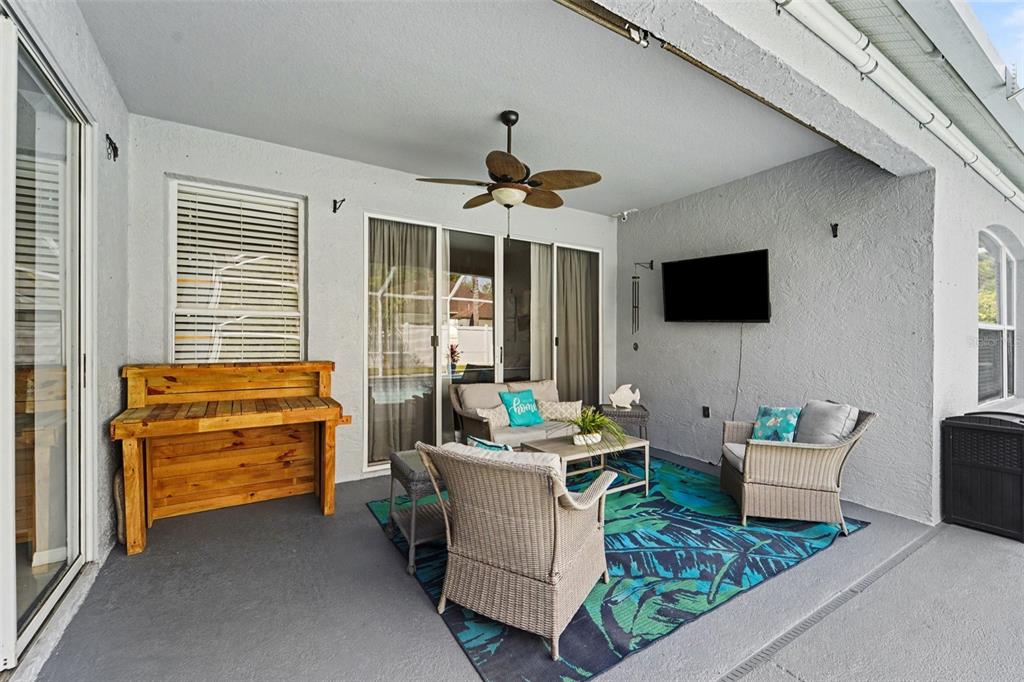 A covered patio features a ceiling fan, outdoor furniture, a rug, and a wall-mounted television — 19717 WYNDHAM LAKES DRIVE, ODESSA, FL