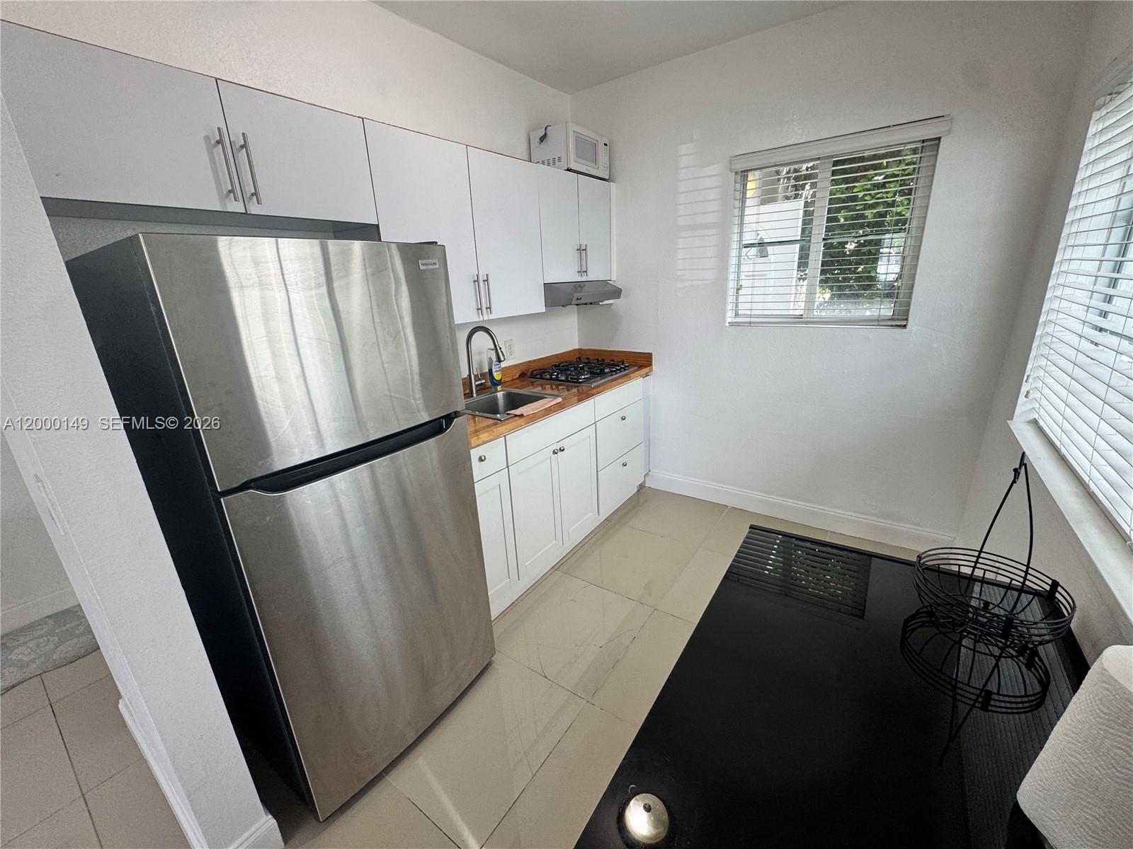 A small kitchen features white cabinets, stainless steel appliances, and a wood-look countertop — 8415 Harding Ave # 9, Miami Beach FL 33141, MIAMI BEACH, FL