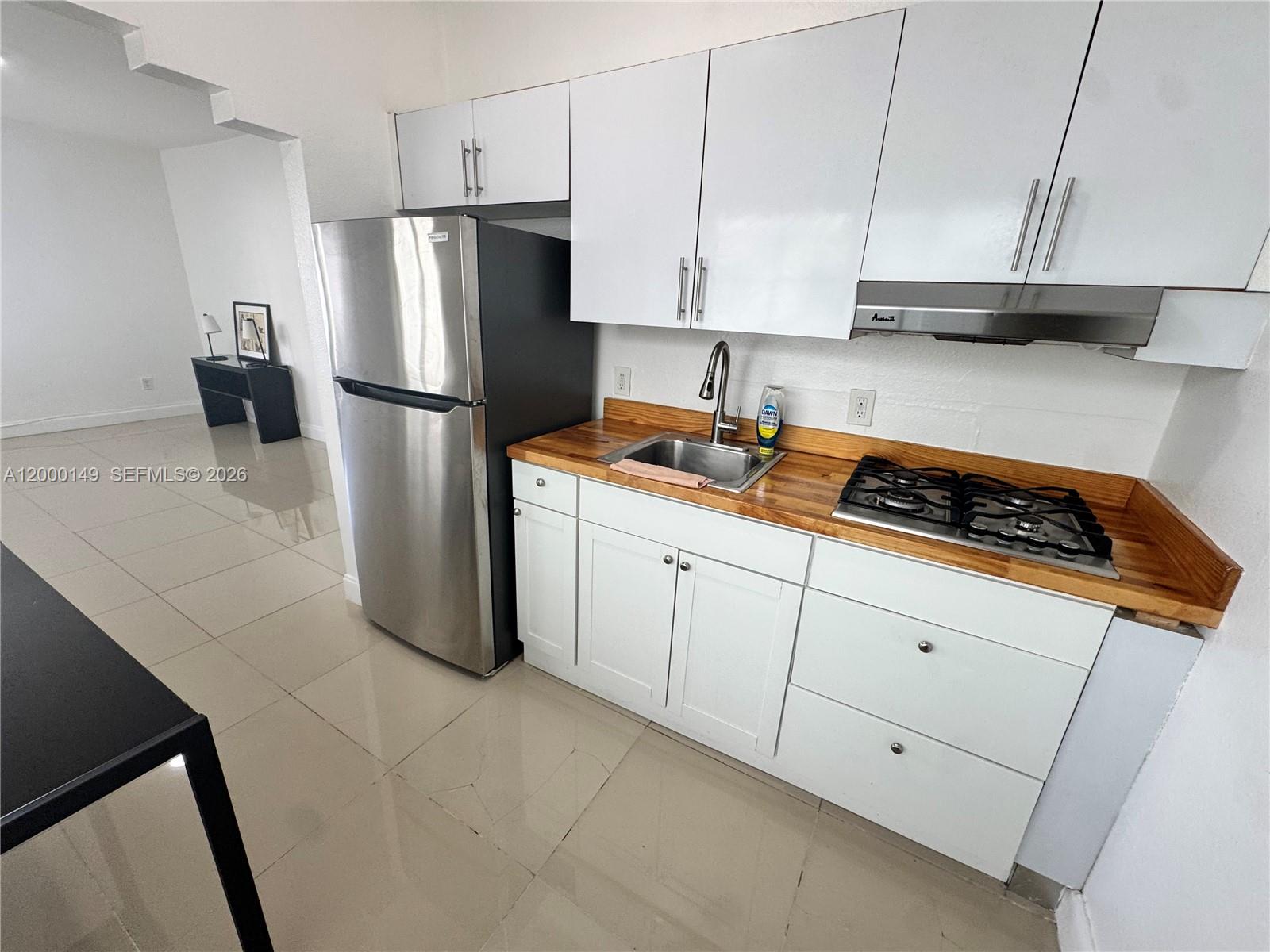 A small kitchen features white cabinets, a stainless steel refrigerator, and a wooden countertop — 8415 Harding Ave # 9, Miami Beach FL 33141, MIAMI BEACH, FL