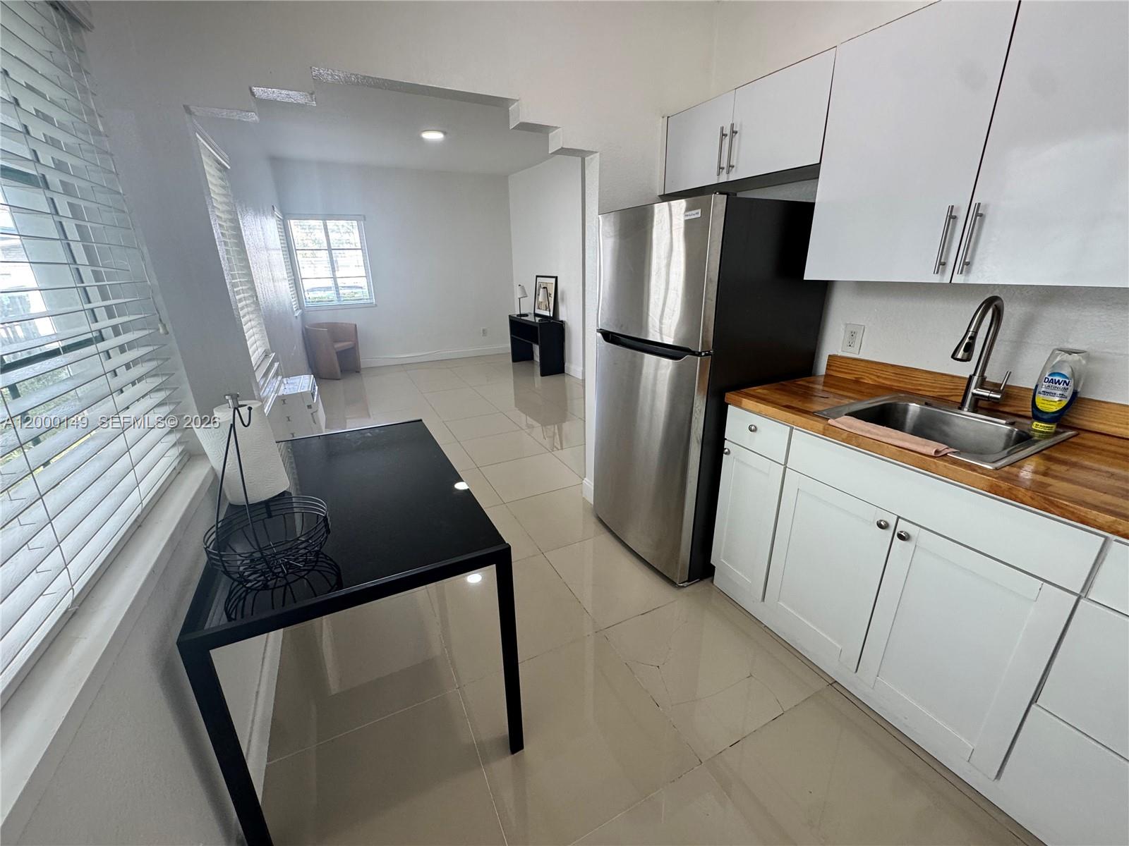 A kitchen with white cabinets, stainless steel appliances, and wood countertops opens to a living area — 8415 Harding Ave # 9, Miami Beach FL 33141, MIAMI BEACH, FL