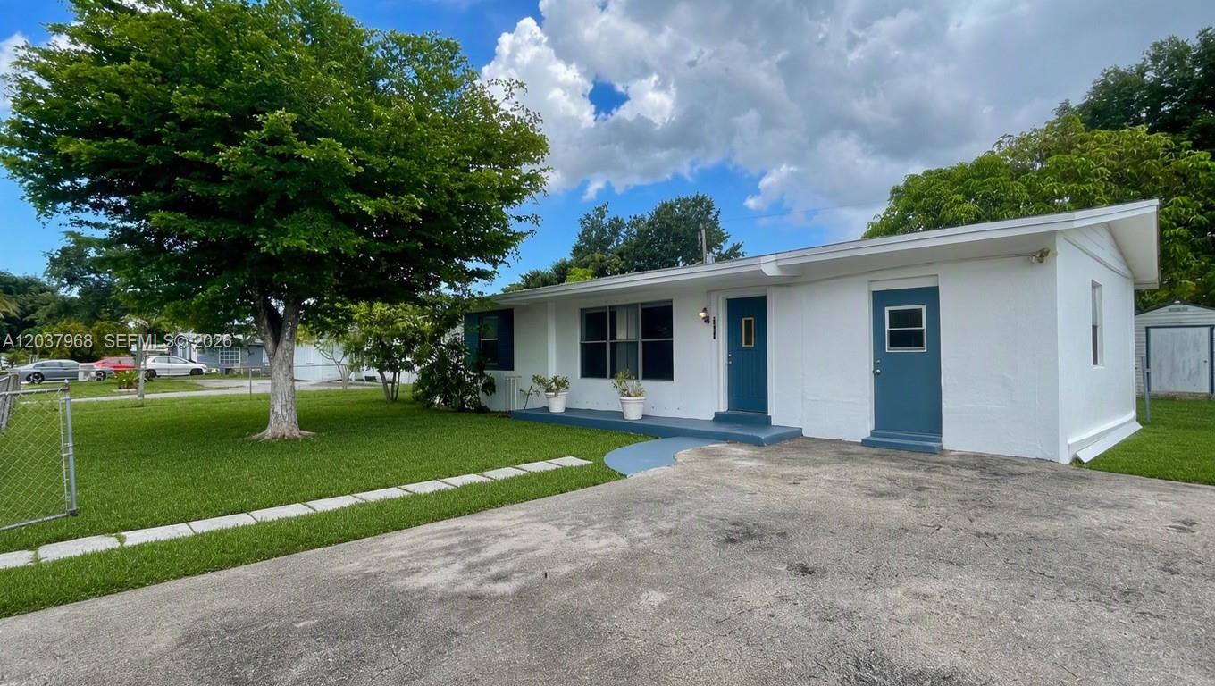 A white, single-story house with a blue door and a concrete driveway — 3460 NW 5th Ct, Lauderhill FL 33311, LAUDERHILL, FL