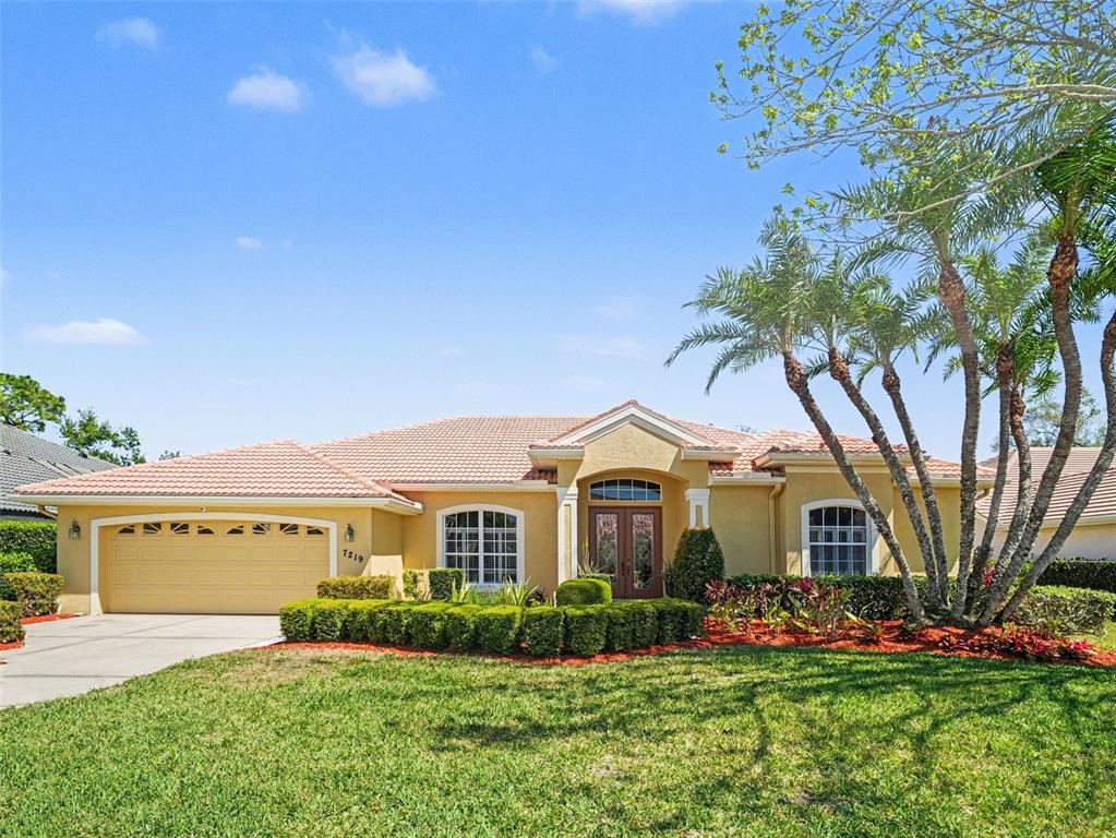 A single-story stucco house with a tile roof, a two-car garage, and palm trees — 7219 COACHLIGHT STREET, SARASOTA, FL