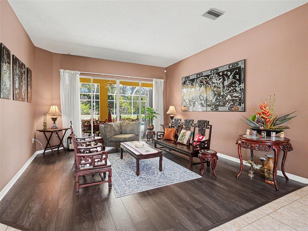A living room features dark wood flooring, Asian-style furniture, and sliding glass doors to a patio — 7219 COACHLIGHT STREET, SARASOTA, FL