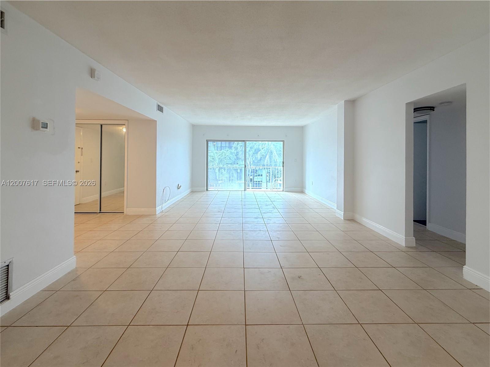 An empty living area features white walls, light-colored floor tiles, and a sliding glass door — 1075 92nd St # 201, Bay Harbor Islands FL 33154, BAY HARBOR ISLANDS, FL