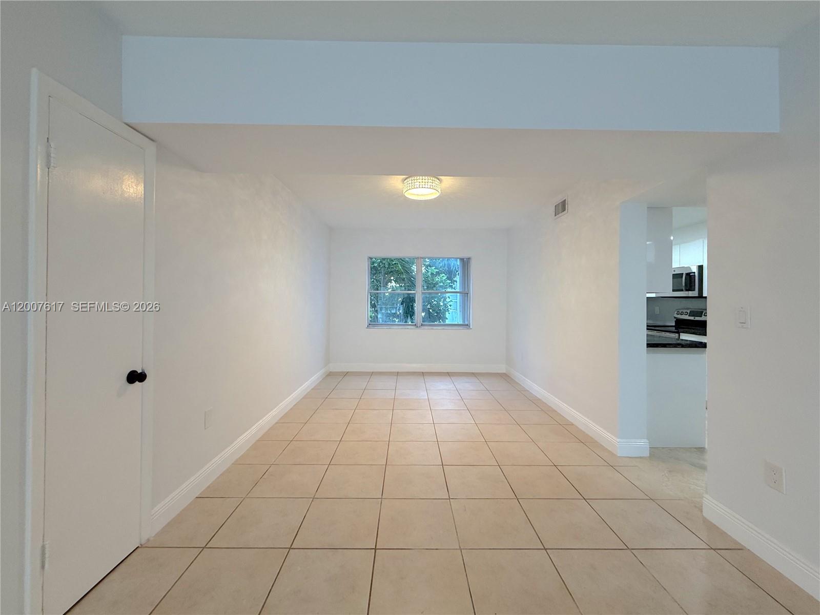 An empty room with white walls, beige tile flooring, a centered window, and a ceiling light — 1075 92nd St # 201, Bay Harbor Islands FL 33154, BAY HARBOR ISLANDS, FL