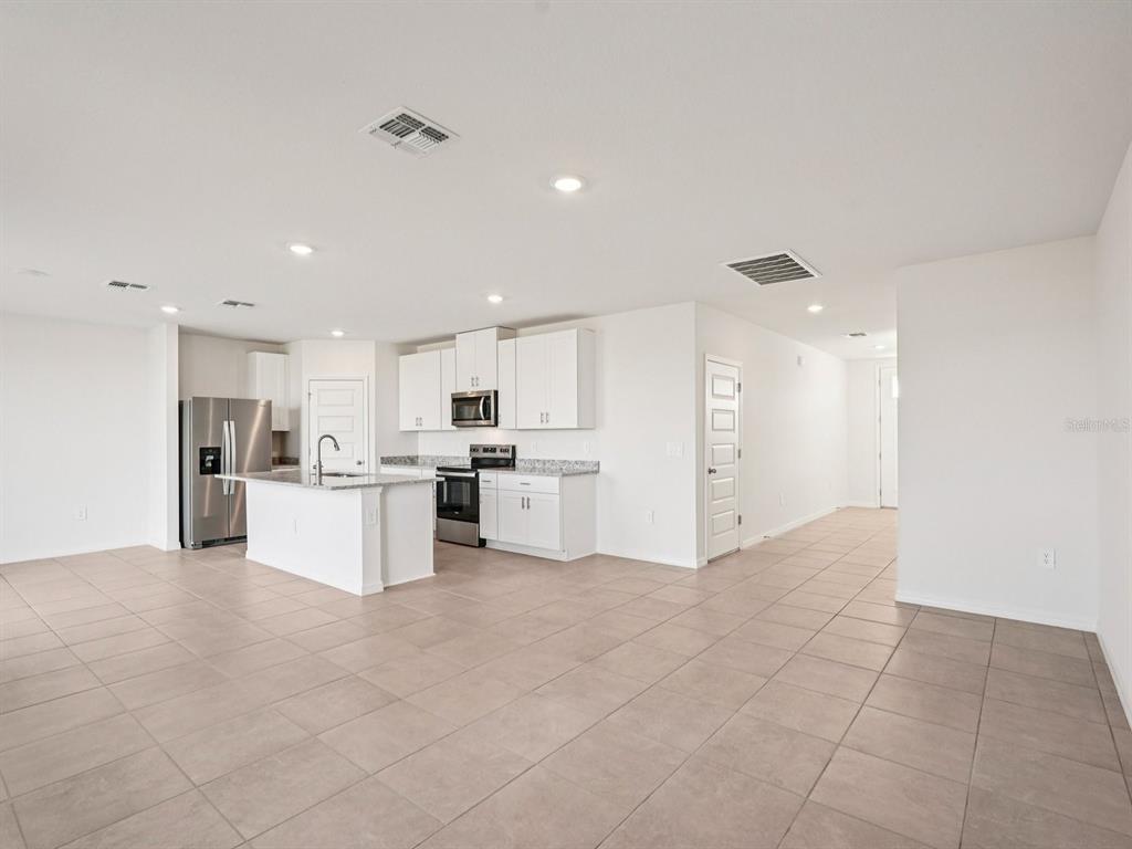 A bright, open-concept kitchen features white cabinets, stainless steel appliances, and light-colored tile flooring — 13613 SHELLMORE AVENUE, PALMETTO, FL