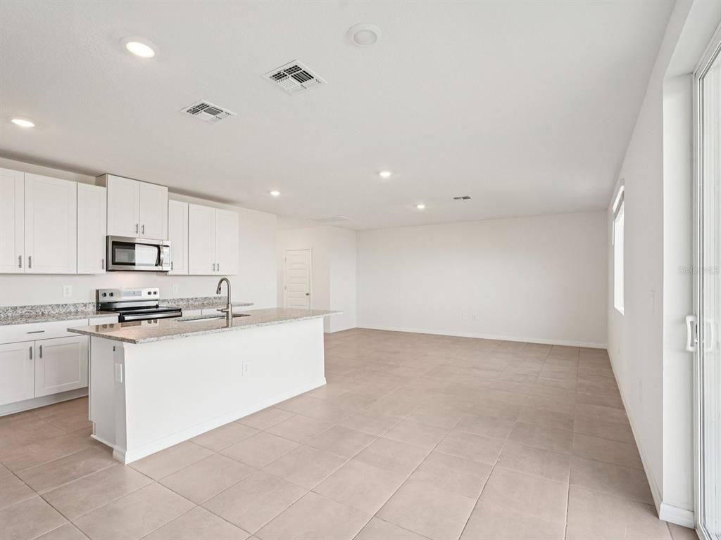 A modern kitchen with white cabinets and a granite island opens into a spacious room — 13613 SHELLMORE AVENUE, PALMETTO, FL