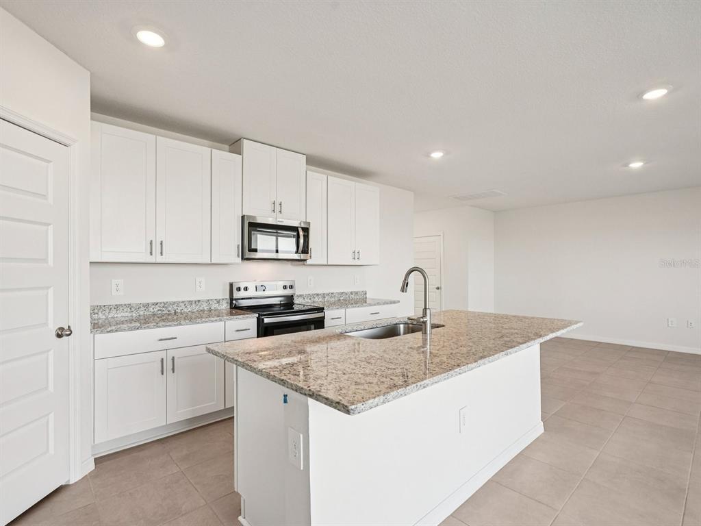 A modern kitchen features white cabinets, granite countertops, a central island, and stainless steel appliances — 13613 SHELLMORE AVENUE, PALMETTO, FL