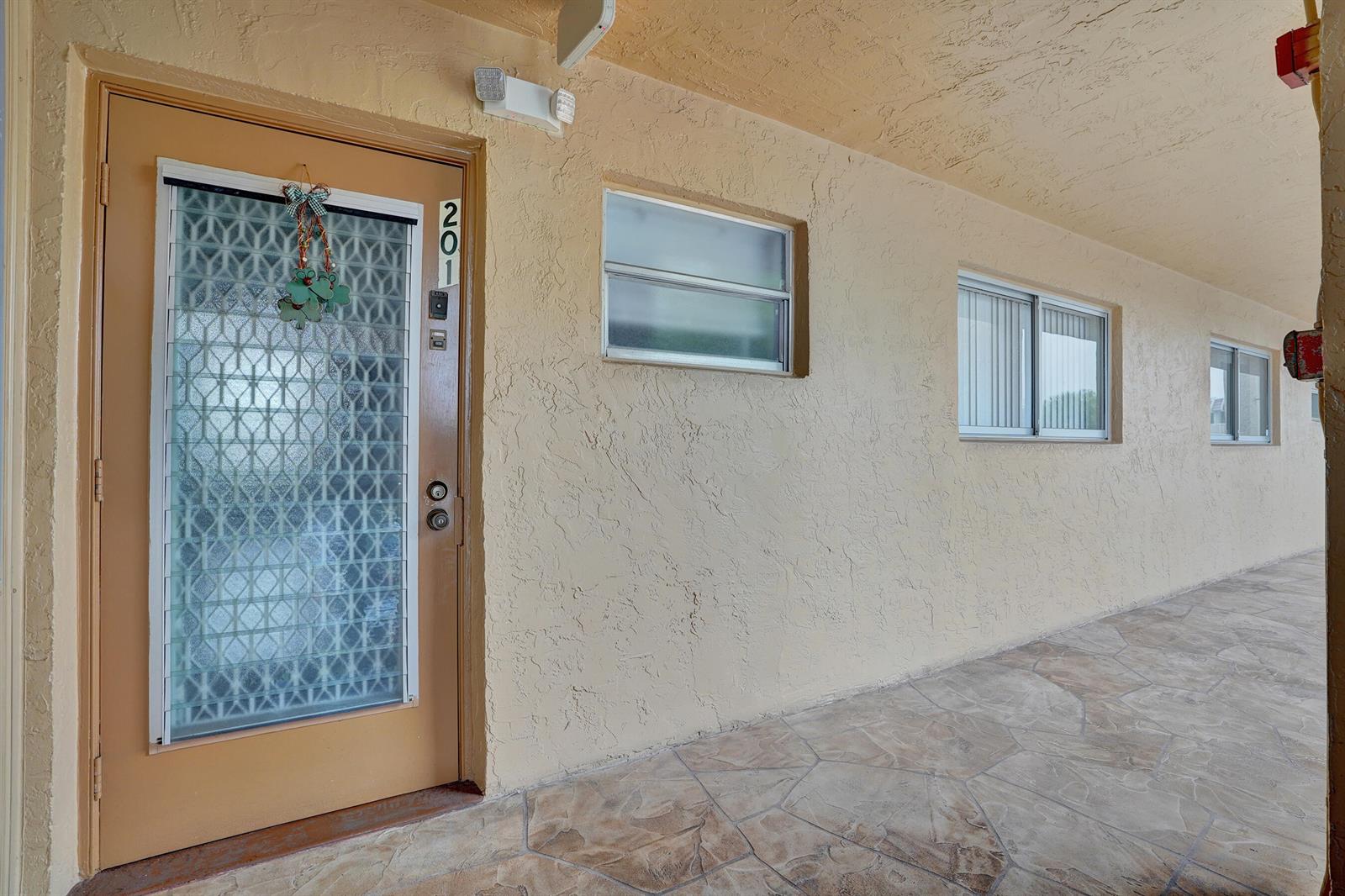 An exterior view of a tan apartment building entrance with a numbered door and windows — 6670 Royal Palm Boulevard # K, Margate FL 33063, MARGATE, FL