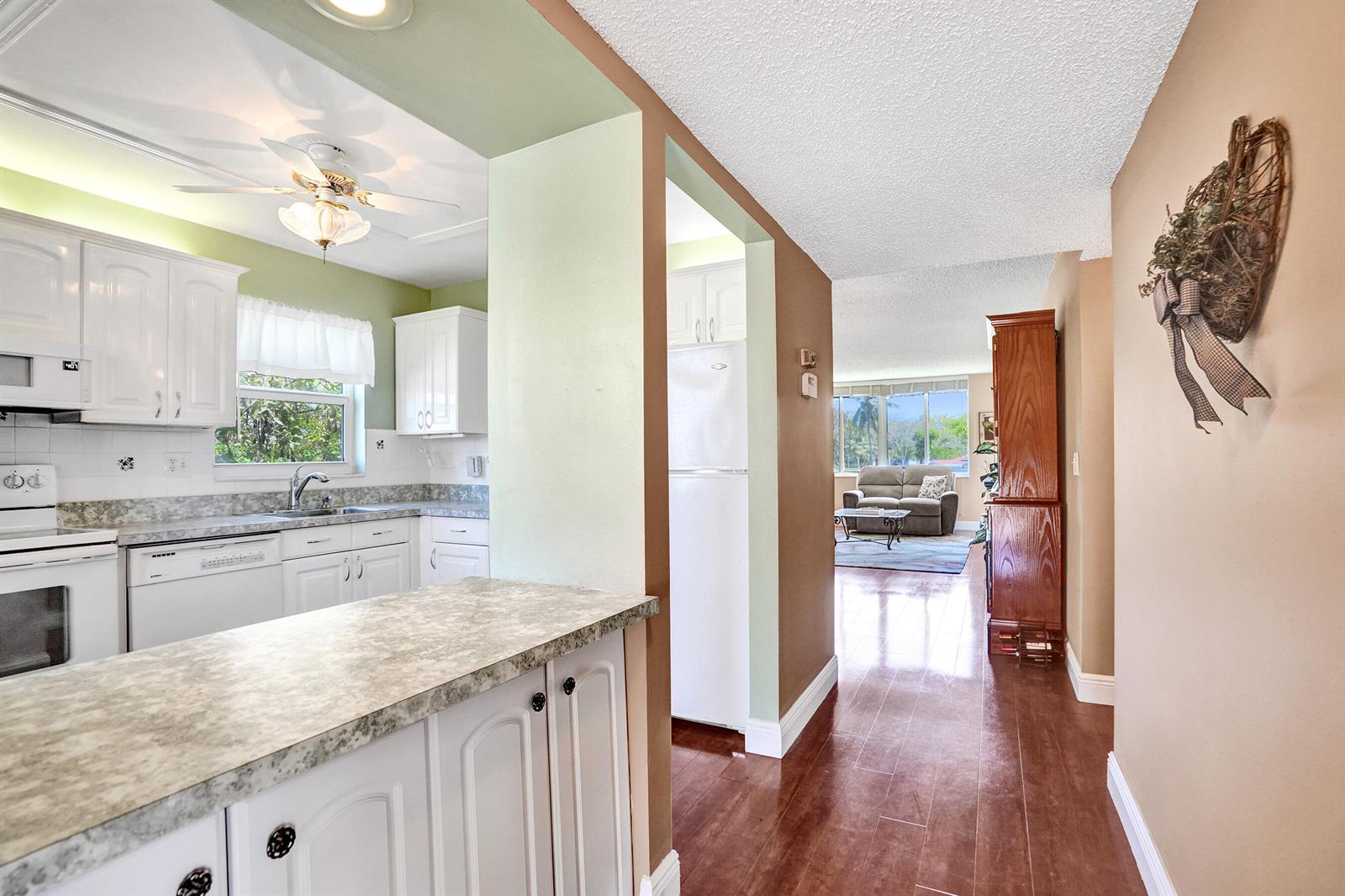 A kitchen with white cabinets and a peninsula opens into a living room with flooring — 6670 Royal Palm Boulevard # K, Margate FL 33063, MARGATE, FL
