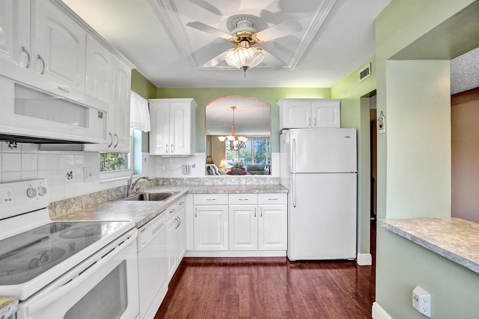 A kitchen with white cabinets, white appliances, green walls, and wood-look flooring — 6670 Royal Palm Boulevard # K, Margate FL 33063, MARGATE, FL