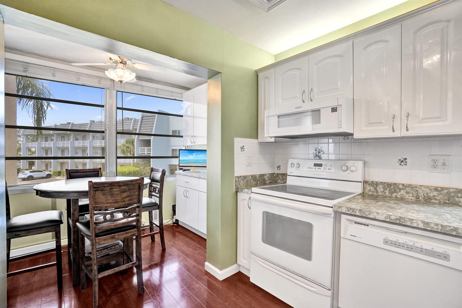 A kitchen with white cabinets, white appliances, and a dining area overlooking an apartment complex — 6670 Royal Palm Boulevard # K, Margate FL 33063, MARGATE, FL