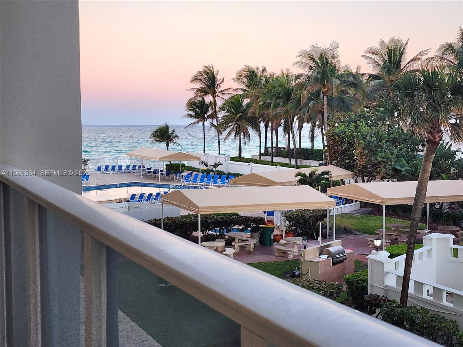 A balcony view overlooks a swimming pool, lounge chairs, cabanas, and the ocean at sunset — 3505 S Ocean Dr # 218, Hollywood FL 33019, HOLLYWOOD, FL