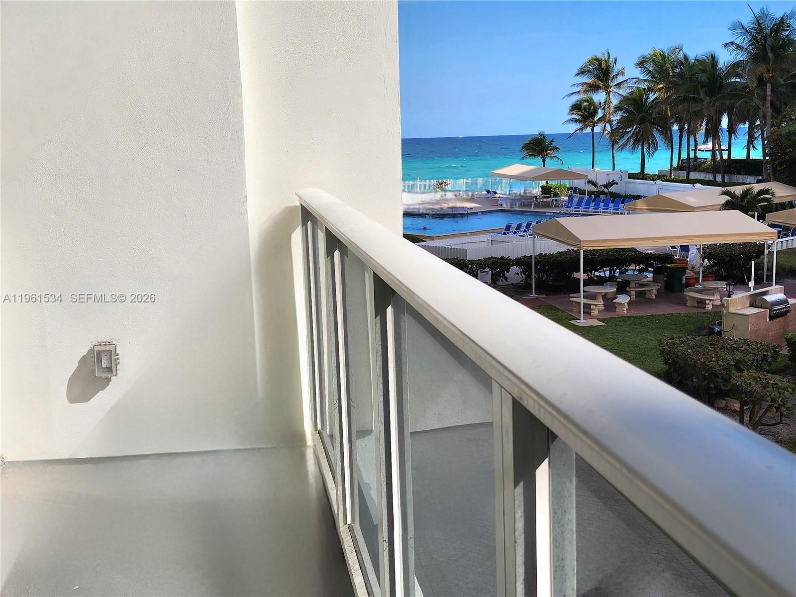 A balcony overlooks a swimming pool, palm trees, and the ocean — 3505 S Ocean Dr # 218, Hollywood FL 33019, HOLLYWOOD, FL