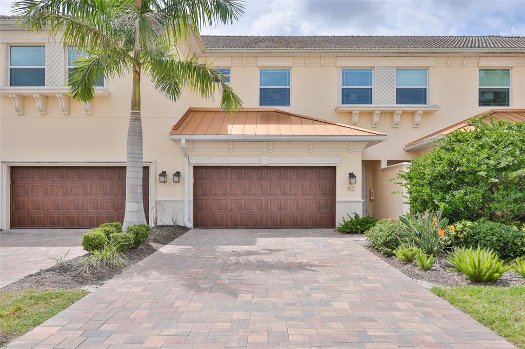 A two-story townhouse exterior features a paved driveway, two garage doors, and a palm tree — 7835 HIDDEN CREEK LOOP UNIT 102, BRADENTON, FL
