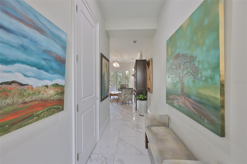 A bright hallway with marble floors, two large paintings, and a bench leads to a room — 7835 HIDDEN CREEK LOOP UNIT 102, BRADENTON, FL