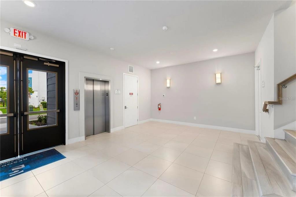 A modern building lobby features a metal elevator, tiled floors, and a staircase — 7740 SANDY RIDGE DRIVE UNIT 211, REUNION, FL